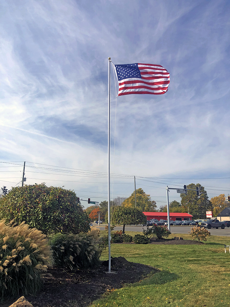 American flag waving on a flagpole against a blue sky with some clouds.